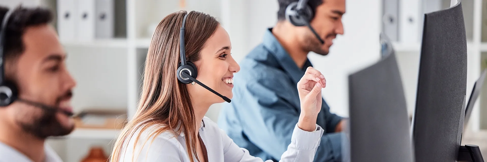 BfV - Investment Research und Backoffice Dienstleistungen Seitliche Ansicht von Kundenbetreuern vor Bildschirmen in freundlichem Gespräch per Headset