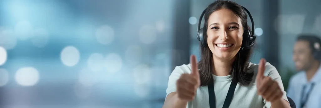 Portrait einer jungen Frau mit Headset, die lächelt und beide Daumen hoch zeigt