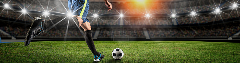 Ein Fußballspieler bereitet sich darauf vor, einen Ball auf einem hell erleuchteten Stadionfeld zu kicken, mit Stadionbeleuchtung und einer großen Menschenmenge im Hintergrund.